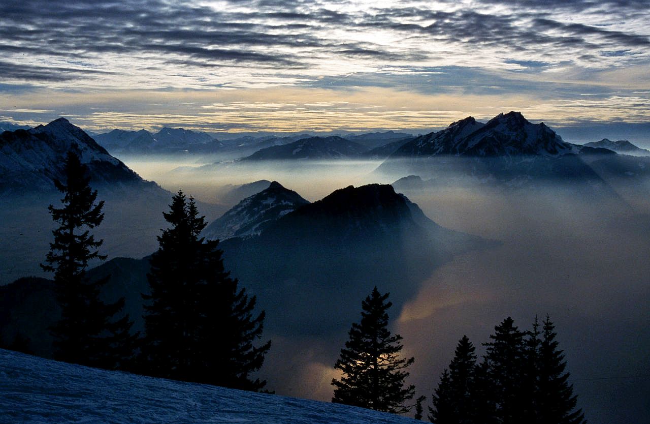 Auf dem Bild geht der Blick vom Winterwanderweg zwischen Rigi Kulm und Rig Scheidegg Richtung Südwesten. In der rechten Bildhälfte dominiert das Pilatus-Massiv, am linken Bildrand das Stanser Horn. In der Bildmitte der deutlich niedrigere Bürgenstock, davor erkennt man einen Teil des Vierwaldstättersees. Im Hintergrund sieht man die Gipfel der Emmentaler Alpen. Der Himmel ist stark bewölkt, die Sonne scheint nur zum Teil hindurch, Dies ergbit aber ein sehr stimmungsvolles Bild, vor allem weil dei Sonnenstrahlen sichtbar sind.