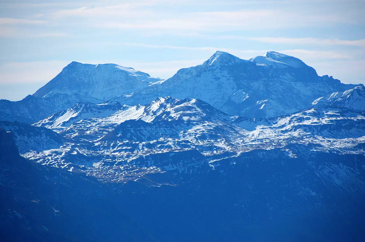 Auf dem Bild geht der Blick vom Chäserrugg auf die drei 3000er im Sardona-Massiv: Trinserhorn links, Piz Sardona und Piz Segnas. Es handelt sich um eine Aufnahme mit dem Teleobjektiv. Im Bildmittelgrund erkennt man die deutlich niedrigeren Berge Schnüerligrat und Rotrüfner. Die Gipfel sind verschneit, auch die niedrigeren. Der Himmel ist blau, aber es hat viele Schleierwolken.