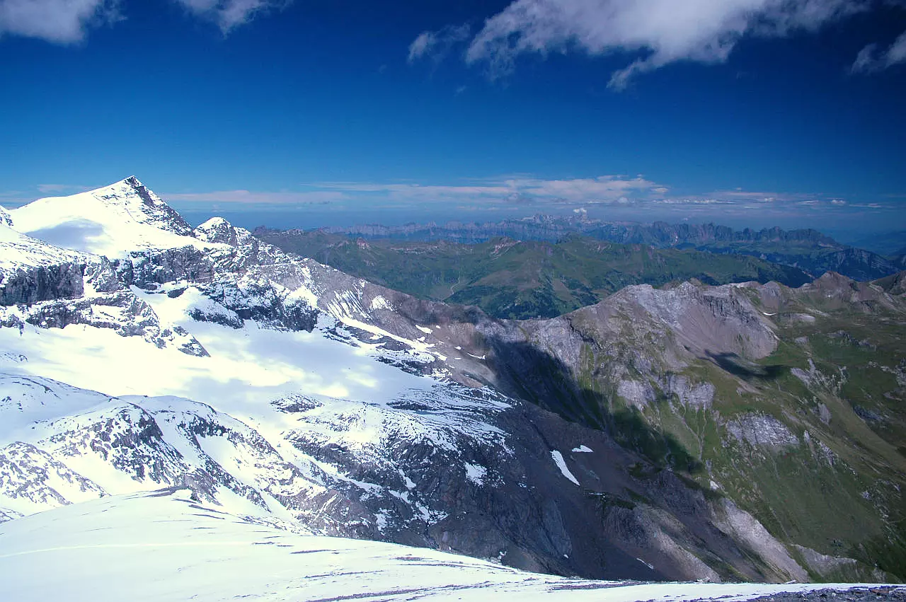 Auf dem Bild geht der Blick vom Trinserhorn Richtung Nordwesten und Norden. Ganz links sieht man den vergletscherten und verschneiten Piz Sardona. Am Gipfelaufbau ist auch die Glarner Hauptüberschiebung zu erkennen. Weiter rechts sieht man im Hintergrund die meist grünen Gipfel der Flumser Berge. Dahinter sieht man am Horizont noch die Kette der Churfirsten und die Alviergruppe. Zwischen beiden ragt noch der Alpstein mit dem Säntis hervor. Der Himmel ist blau, es hat wenige Quellwolken und am Horizont Schleierwolken.