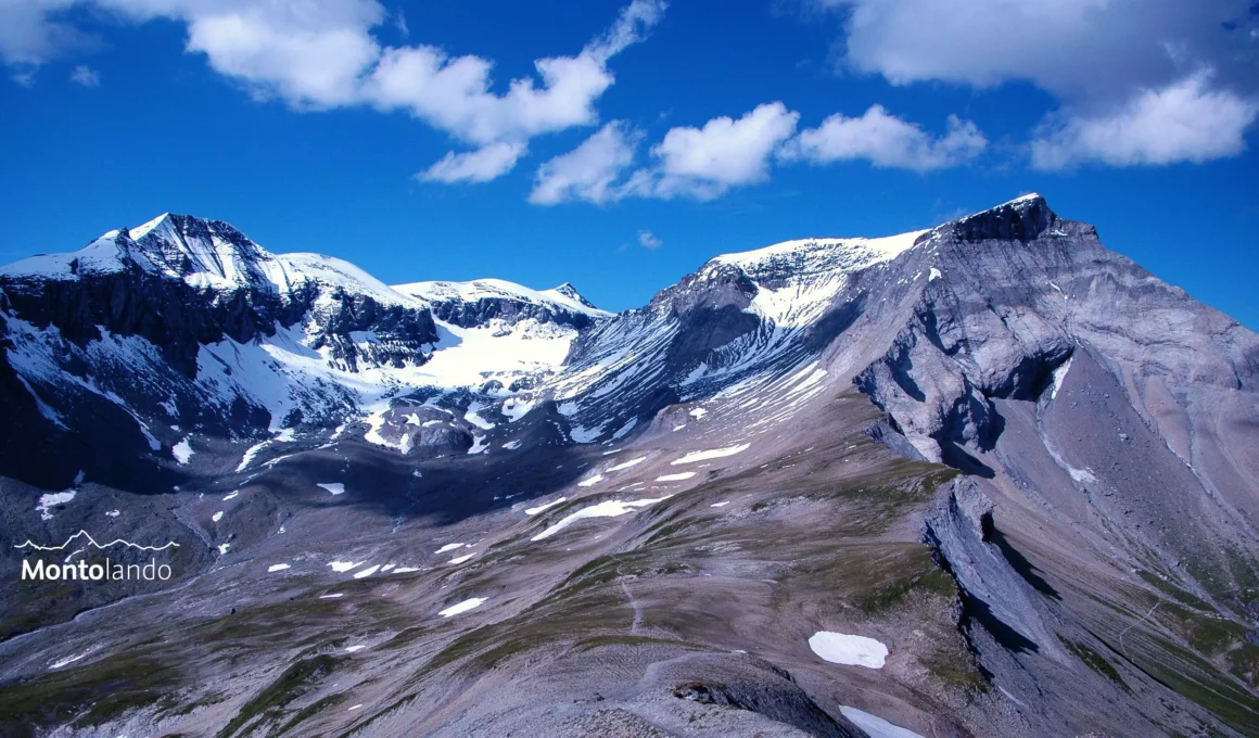 Auf dem Bild geht der Blick vom Fil de Cassons nach Norden auf die drei 3000er Piz Segnas links, Piz Sardona im Hintergrund und Trinserhorn rechts. Unter dem Trinserhorn sind im Vordergrund der Sattel der Fuorcla da Raschaglius und der Weg zu sehen. Am Piz Segnas und am Trinserhorn sieht man die Linie der Glarner Hauptüberschiebung. Links unten ist noch ein Teil des Oberen Segnasboden sichtbar. Die Gipfel sind zum Teil mit Neuschnee bedeckt. Der Himmel ist blau, es hat ein paar kleine Wolken.