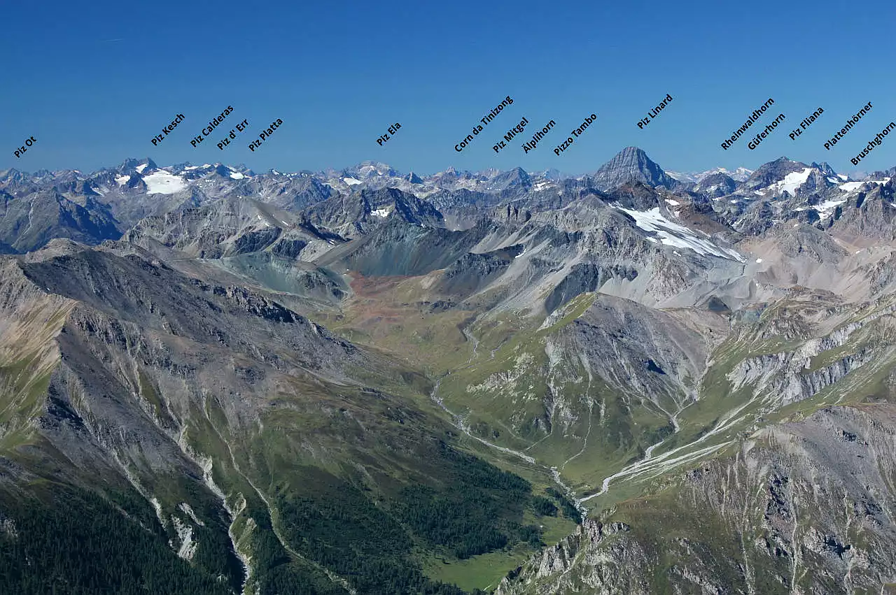 Auf dem Bild geht der Blick vom Muttler in Richtung Südwesten über die Bergwelt Graubündens, die Bündner Alpen. Man sieht viele bedeutende Gipfel der Albulagruppe (Piz Ot, Piz Kesch, Piz Ela) links und in der Mitte. Rechts die Silvretta mit Piz Linard und Piz Fliana. Dazwischen schauen noch der Pizzo Tambo am Splügenpass, die Adula mit Rheinwaldhorn und Güferhorn und das Bruschghorn über der Viamala hervor. Es ist ein außergewöhnlich klarer Tag. Der Himmel ist blau und wolkenlos.