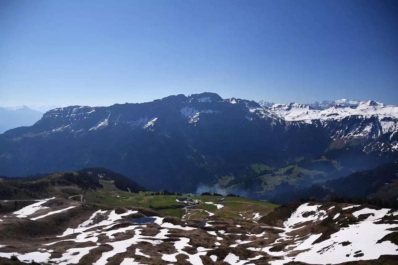 Auf dem Bild geht der Blick vom Gipfel des Ziger über das Schilstals hinweg zum Kamm des Hochfinslers, der genau in der Bildmitte zu sehen ist. Nach links zieht sein Kamm über Hochgamatsch und Steingässler zur Guscha, von der der Kamm ins Tal absinkt. Rechts im Hintergrund sieht man die noch schneebedeckten Gipfel Sazmartinshorn, Guli, Schnüerligrat und Ringelspitz. Auch im Vordergrund unter dem Ziger sieht man im Bereich der Skilifte noch einige Schneefelder. Der Himmel ist blau und wolkenlos.