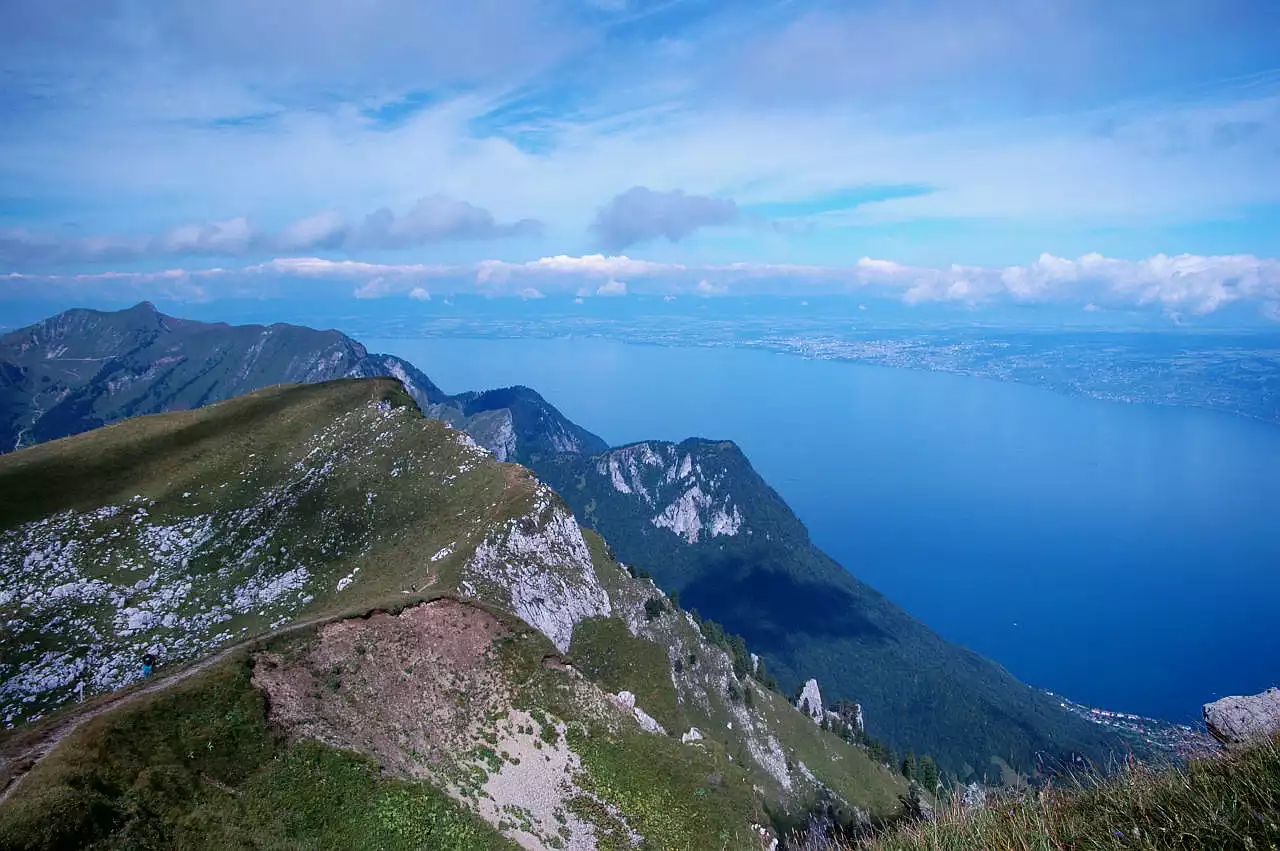 Auf dem Bild geht der Blick knapp unterhalb von Le Grammont auf den Genfersee, den Lac Léman. Auf der anderen Seite erkennt man Lausanne und dahinter den Jura, dessen Gipfel allerdings in Wolken stecken. Links sieht man über einen Vorgipfel des Grammont hinweg auf den Pic Boré, der bereits in Frankreich liegt. Rechts unten erkenn man noch die Ortschaft St. Gingolph am Genfersee. Der Himmel ist blau, aber es hat viele Schleierwolken und zum Teil auch Quellwolken.