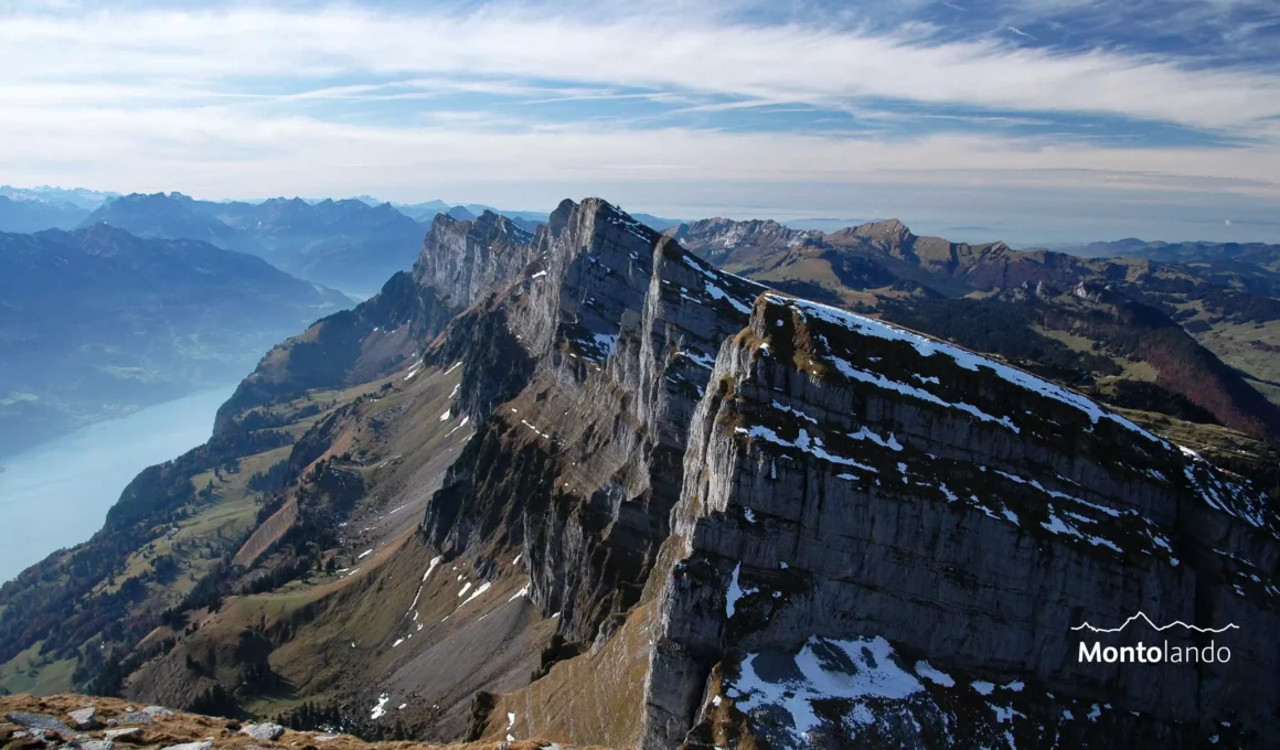 Auf dem Bild geht der Blick vom Hinderrugg, dem höchsten Gipfel der Churfirsten, Richtung Westen zu den anderen Churfirsten. Sie fallen nach Süden (links) mit prallen Seilwänden zum Walensee ab, den man am linken Bildrand noch sieht. Dahinter sieht man noch einige Gipfel der Glarner Alpen. Nach Norden (rechts) dachen sie sich mit sanfteren Rücken ab. Dort sieht man im Hintergrund noch den Speer und in der Ferne die Hügel im Zürcher Oberland. Der Himmel ist blau und mit schönen Schleierwolken verziert.