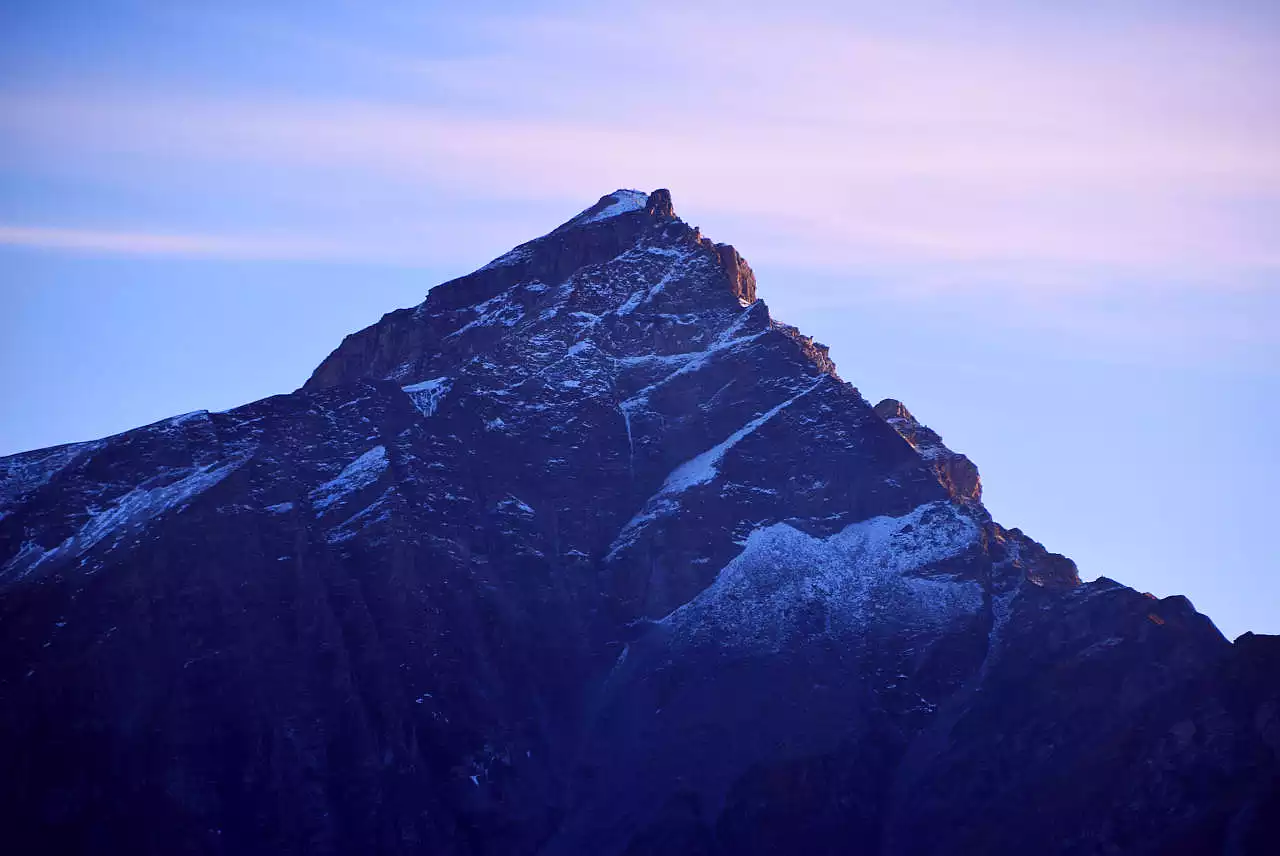 Auf dem Bild sieht man den Piz Beverin von Norden, knapp unterhalb der Präzer Höhi. Man blickt direkt in die Nordwand, die ebenso im Schatten liegt wie die Ostseite (links). Nach rechts unten zieht der Nordwestgrat, der wie die Westflanke noch von der Sonne beschienen wird. Der Himmel ist hellblau, die Schleierwolken spiegeln die Abendröte.