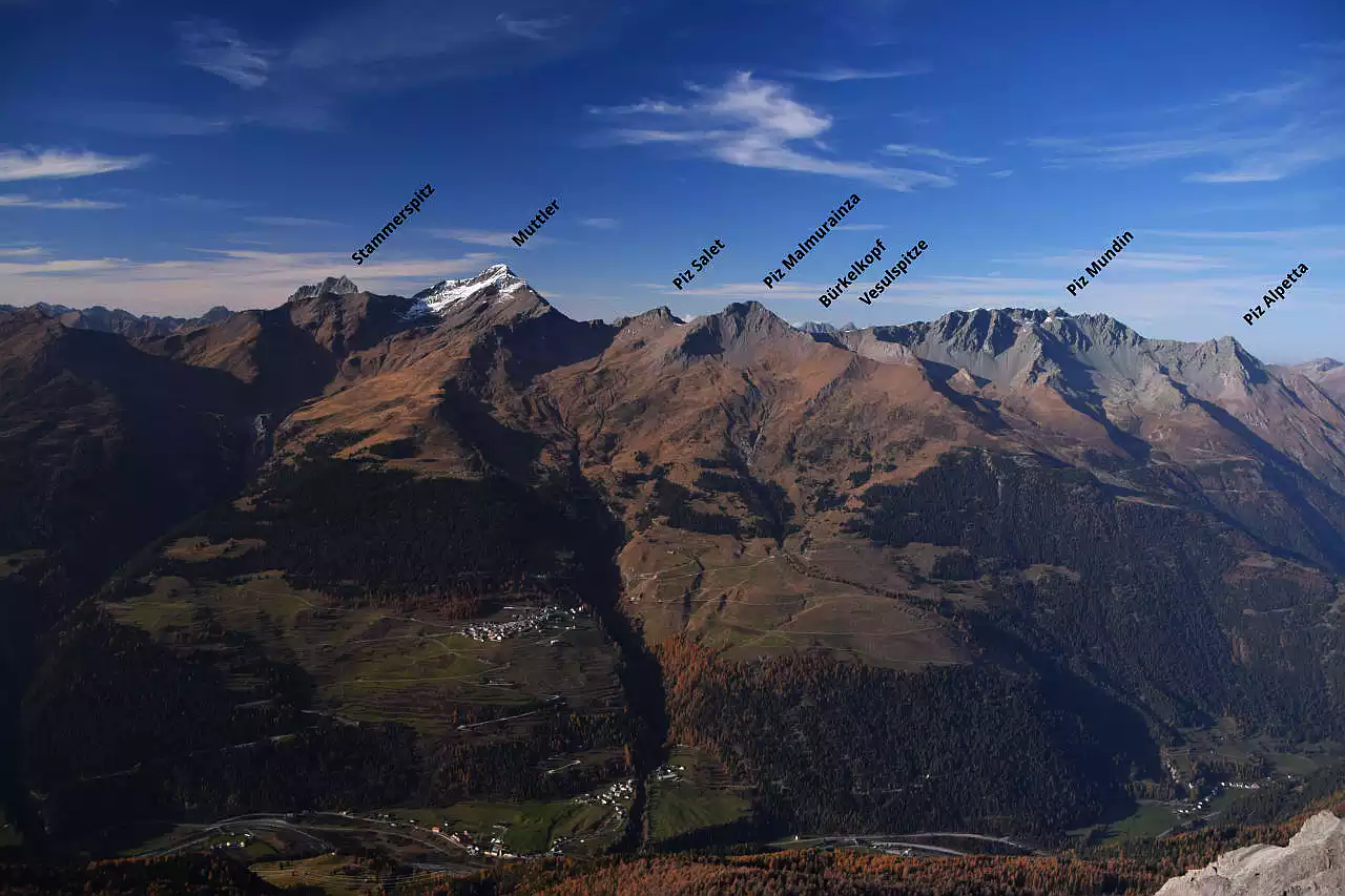 Auf dem Bild geht der Blick vom Piz Lad über das Unterengadin hinweg zu den Gipfeln der Samnaungruppe, aus der besonders der zum Teil schneebedeckte Muttler herausragt. Die bedeutendsten Gipfel sind auf dem Bild beschriftet. Unter den Gipfeln erkennt man einige Unterengadiner Dörfer wie Tschlin und Strada. Der Himmel ist blau und wird von Schleierwolken verziert.