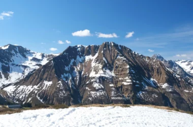 Auf dem Bild geht der Blick vom Anstieg zum Steinmandl bei Schoppernau Richtung Süden zur Üntschenspitze. Man sieht die breite und steile Nordflanke, in deren Gräben noch Schneefelder liegen. Links sieht man die Güntlespitze, unter deren Gipfel noch viel Schnee liegt. Rechts sieht man noch die Hochkünzelspitze und Schöneberg im Lechquellengebirge. Der Himmel ist blau, es hat Schleierwolken und ein paar ganz kleine Schönwetterwölkchen.